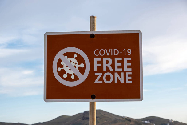 Covid szabad zóna jel. COVID 19 INGYENES ZONE szöveges címke hirdetőtáblán, kék ég háttér. Fertőtlenített területek, csak vakcinázott fogalom - Fotó, kép