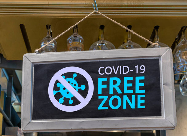 Знак свободной зоны Ковида. COVID 19 FREE ZONE текстовая этикетка висит, размытый фон бара паба. Продезинфицированные участки, вакцинированная только концепция - Фото, изображение