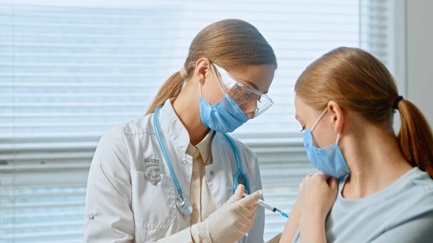 Blondynka medyczna w jednorazowej masce do twarzy i okularach wypełnia strzykawkę szczepionką przeciw zakażeniu wirusem kovidu - Zdjęcie, obraz
