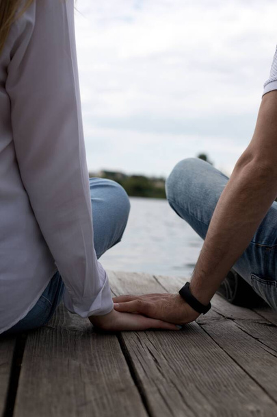 Egy fiú és egy lány fogják egymás kezét, és leülnek a folyó mellé.  - Fotó, kép