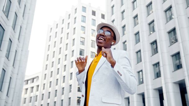 Afrikkalainen amerikkalainen esiintyjä valkoisessa puvussa ja keltainen t-paita tanssii neliöllä korkeiden megalopolis-rakennusten joukossa - Valokuva, kuva
