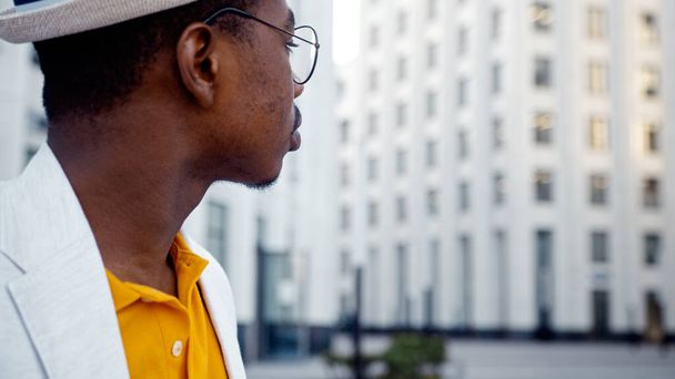 アフリカ系アメリカ人の男性が街の通りに立ってスマートフォンで地元の高層オフィスビルの写真を撮っています - 写真・画像
