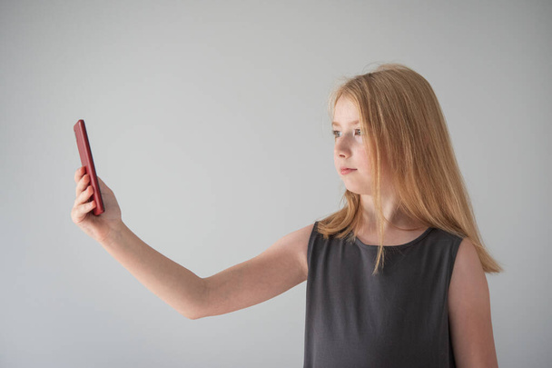ein Mädchen in grauem Kleid und mit einem Handy auf dem grauen Hintergrund macht Fotos - Foto, Bild