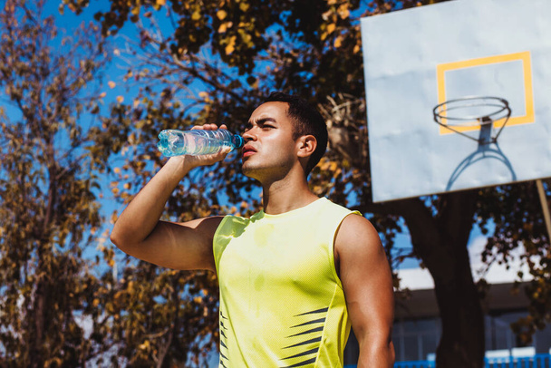 Porträt eines jungen lateinamerikanischen Mannes, der nach dem Training in Mexiko eine Flasche Wasser trinkt - Foto, Bild