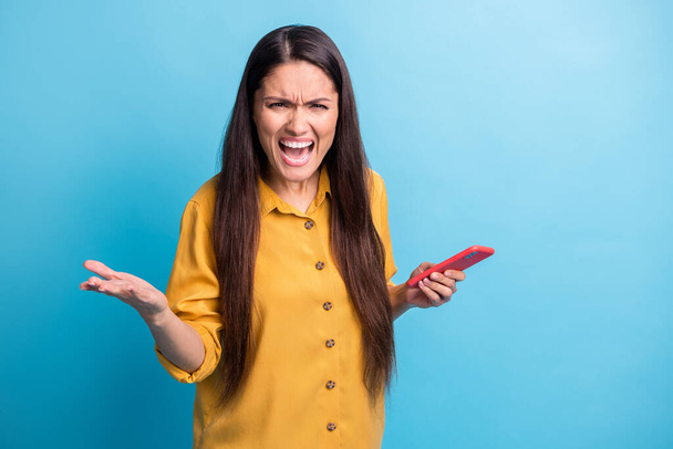 Photo portrait of angry woman holding smartphone shouting having conflict unhappy isolated on vibrant blue color background - Foto, imagen