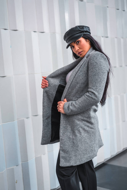 Street style of a young brunette Latina with a leather hat and a gray raincoat - Foto, imagen