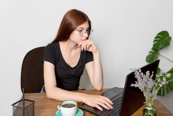 Una joven caucásica con gafas mira a la pantalla del ordenador portátil. Buscando un trabajo o navegar por la red - Foto, Imagen