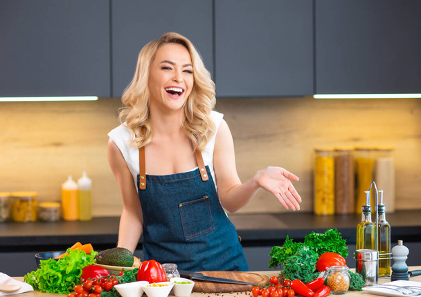 Young woman prepares food and hosts a cooking show. The blogger streams from modern kitchen. Vegetarian healthy food preparation. - Foto, Imagen