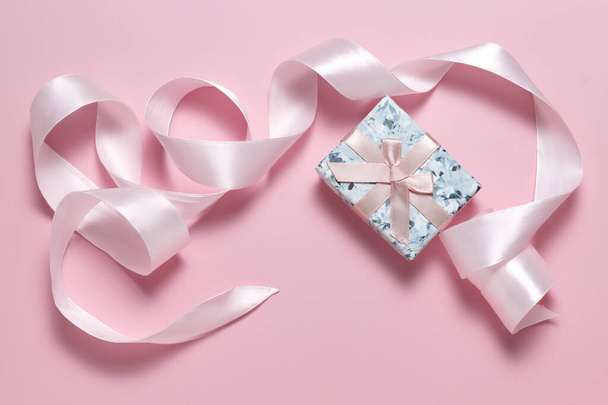 Маленькая подарочная коробка с бантом и розовой лентой для упаковки подарков на розовом фоне - Фото, изображение