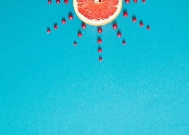 Zon gemaakt van rode sappige grapefruit en cranberry op felblauwe achtergrond. Creatief zomerontwerp. Minimale vlakke lay. - Foto, afbeelding