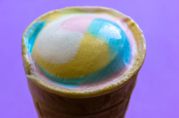 上からの紫色の背景のビューにワッフルカップの中に多色のクールなアイスクリーム、フラットです。2021年夏の流行の色-パステルブルー、ピンク、黄色。高カロリーの甘いスナック。夏の食のコンセプト. - 写真・画像