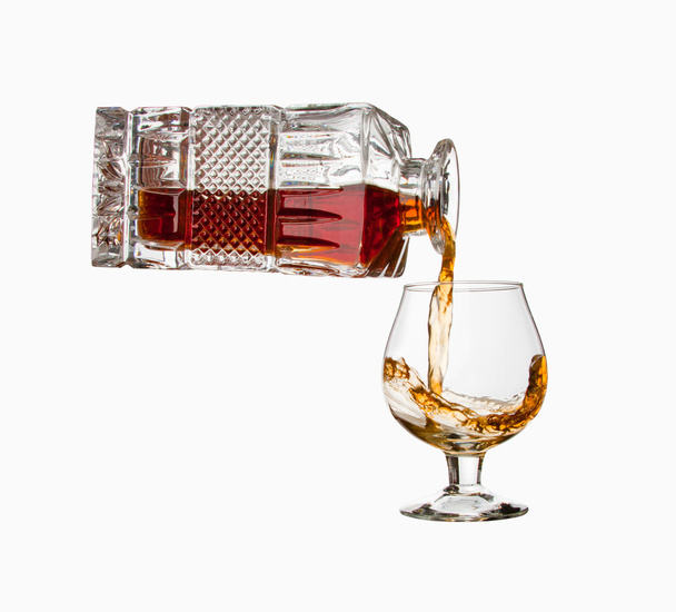 Cognac aus der Flasche in ein Glas gießen. isoliert - Foto, Bild