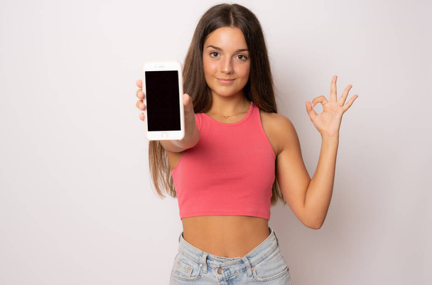 Portrait of a smiling young woman showing blank screen mobile phone isolated over white background - Foto, Imagem