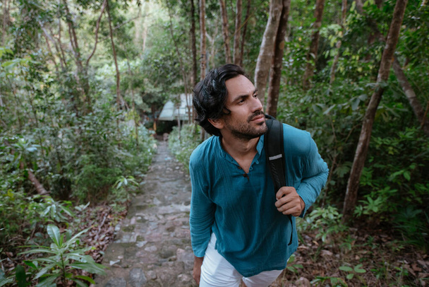 Male tourist climbs up the mountain in the tropical forest. Young handsome caucasian guy walking up the steps through the green thickets on a tropical island - Foto, Imagen