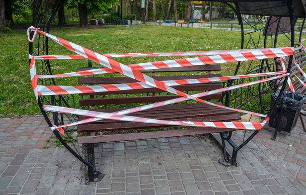 Bench fenced with red-white barrier tape. The access is denied during coronavirus COVID-19 pandemic. Quarantine period concept - Photo, Image