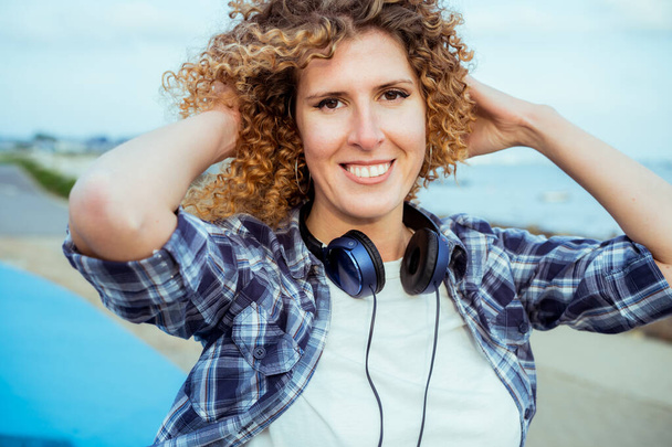 Close up Portrait of smiling curly hair caucasian woman with large headphones walking outdoor. Enjoy the moment and music. Freedom and happiness, simple pleasures concept. - Foto, Imagen