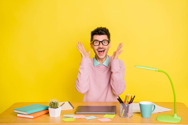 Photo of young handsome excited crazy smiling cheerful man studying at table isolated on yellow color background - Photo, image