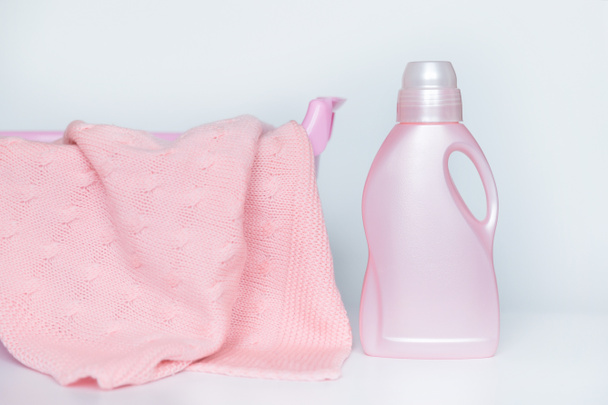 Una botella con un detergente para lavar cosas de lana en el fondo de un lavabo con una manta de punto.  - Foto, imagen