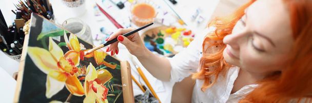 Woman sits at home in front of an easel and draws - 写真・画像
