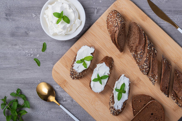 Home made bread on a wooden cutting board with curd cheese and ricotta and herbs. Decorated with mint	 - Foto, Imagen