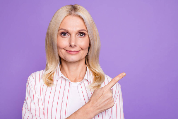 Photo of charming pretty mature woman dressed pink shirt pointing finger empty space isolated purple color background - Foto, Imagem