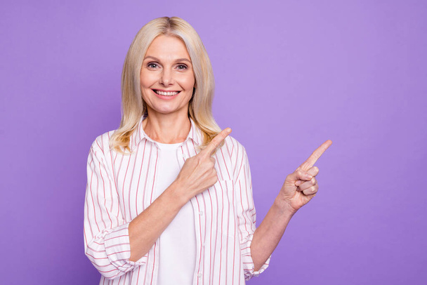 Photo of pretty sweet mature woman dressed pink shirt pointing two fingers empty space isolated purple color background - Foto, Imagen