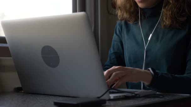 Giovane donna con auricolari lavora sul computer portatile in treno primo piano - Filmati, video