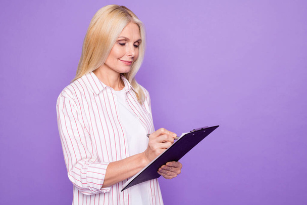 Photo of cute charming mature woman dressed pink shirt writing clipboard empty space isolated purple color background - Zdjęcie, obraz