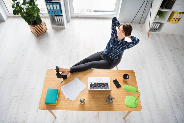 Top above high angle view of attractive cheerful dreamy girl sitting in chair putting legs on table resting at workplace workstation indoors - Foto, Imagem