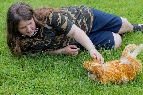 Girl lying on the green grass with a cute padovana chicken. - Photo, Image