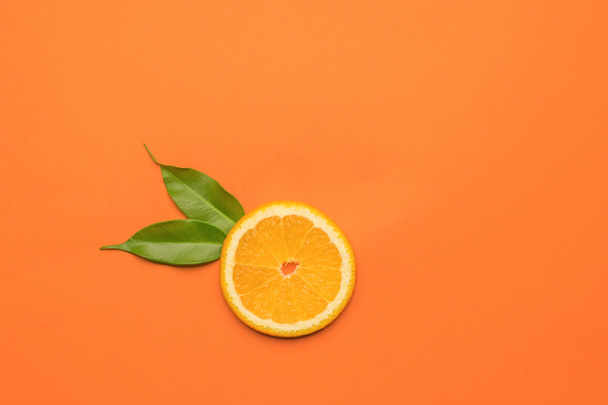 オレンジの背景に2枚の葉と1枚のオレンジ。人気のトロピカルフルーツです。平敷. - 写真・画像