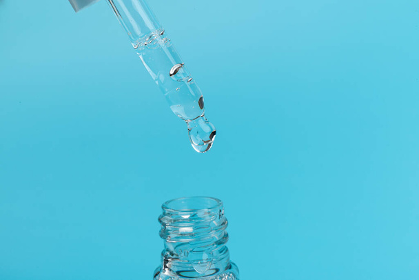 Kosmetik- oder medizinische Glasflasche mit Pipette auf blauem Hintergrund, in Nahaufnahme. Hautpflegekonzept.  - Foto, Bild