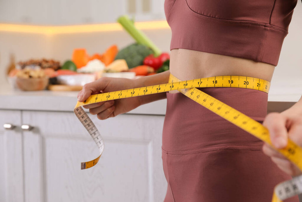 Woman with measuring tape in kitchen, closeup. Keto diet - Photo, image