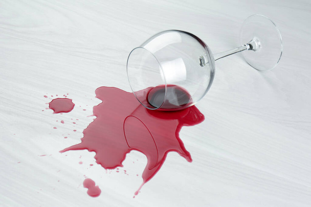 Overturned glass and spilled wine on white wooden table - Foto, afbeelding