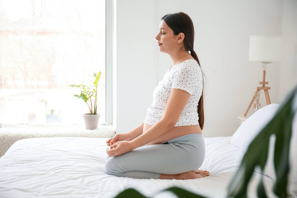 Young pregnant woman practicing yoga in bedroom - Fotó, kép