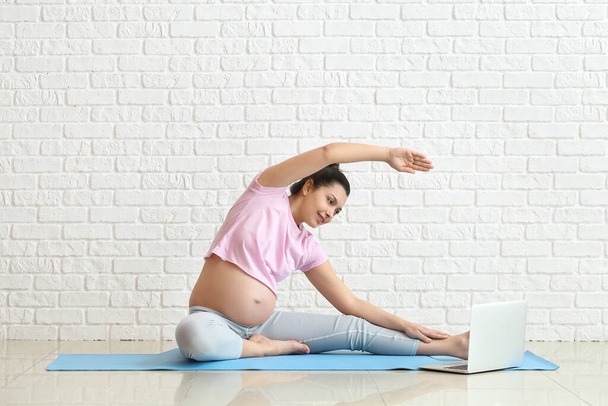 Young pregnant woman practicing yoga near brick wall - Фото, зображення