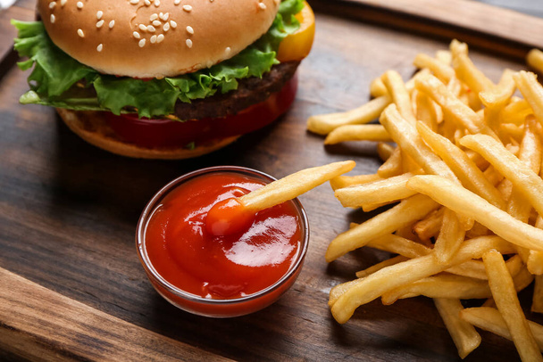 Sabrosas papas fritas, salsa de tomate y hamburguesa sobre tabla de madera - Foto, Imagen