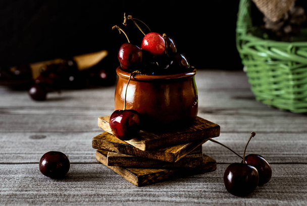 The ripe cherries in the small deep container on the stacked wooden pieces - Foto, Bild