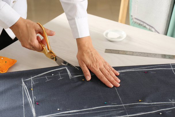 Seamstress cutting fabric following chalked sewing pattern at table in workshop, closeup - Foto, Imagen