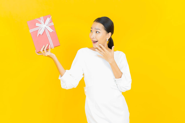 Portret mooie jonge aziatische vrouw glimlach met rode geschenkdoos op kleur achtergrond - Foto, afbeelding