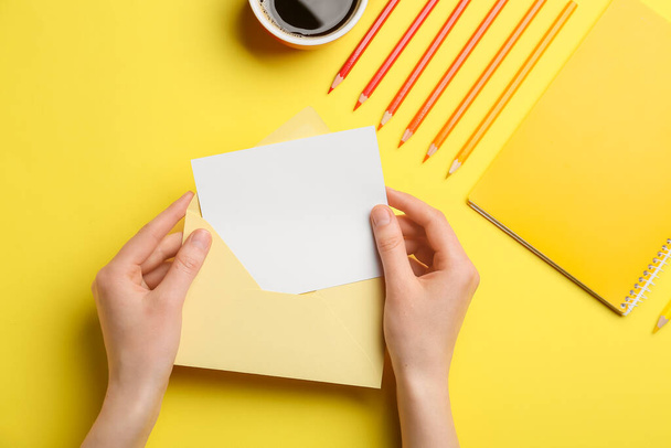 Руки женщины с чистым листом бумаги, конверта и канцелярских принадлежностей на цветном фоне - Фото, изображение