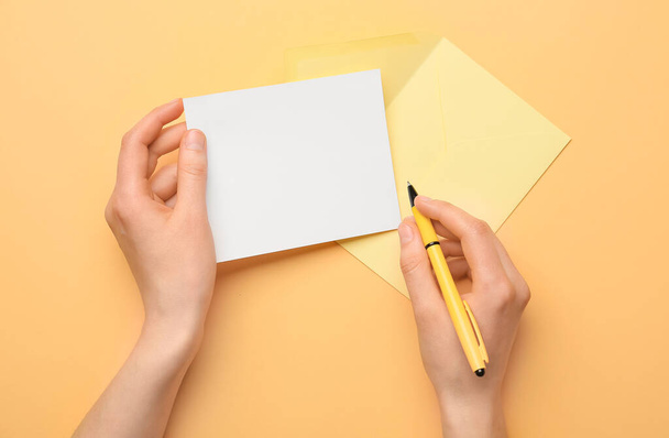 Mãos femininas com folha em branco de papel, envelope e caneta sobre fundo de cor - Foto, Imagem