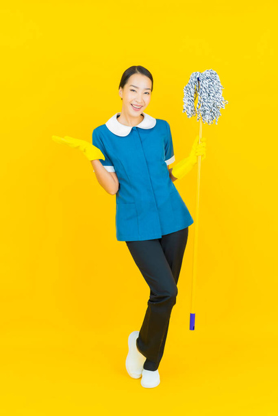 Portrét krásná mladá asijská žena služka a úklid úsměv s akcí na žlutém pozadí - Fotografie, Obrázek