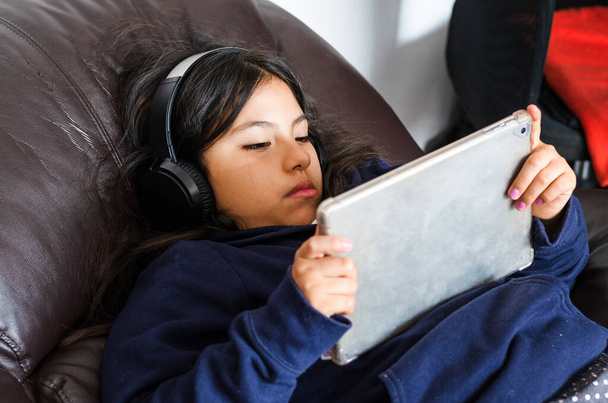 Small girl school pupil wears headphones conference calling studying online with remote tutor from home. - Photo, Image