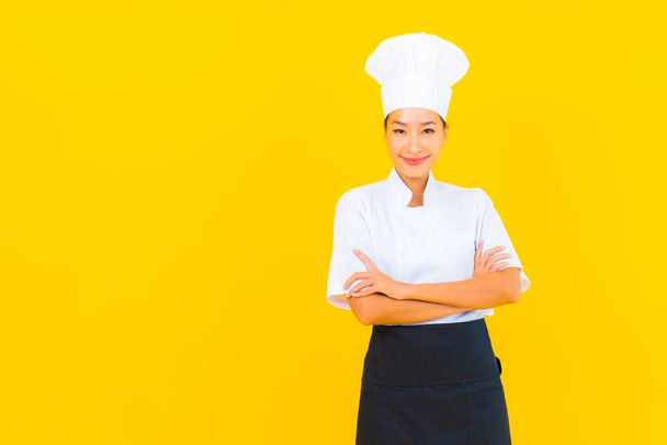 Portrait beautiful young asian woman in chef or cook uniform with hat on yellow isolated background - Foto, Bild