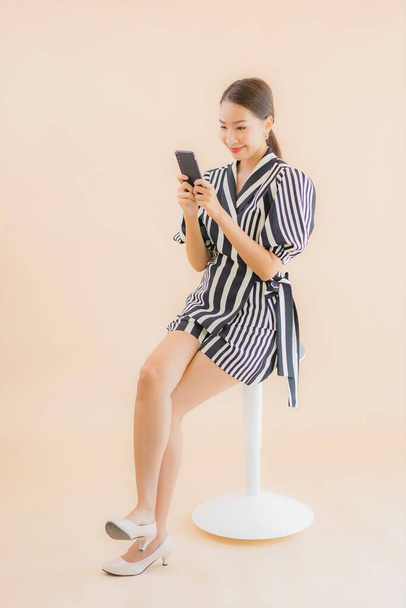 Πορτρέτο όμορφη νεαρή Ασιάτισσα γυναίκα με έξυπνο κινητό τηλέφωνο σε καφέ φόντο - Φωτογραφία, εικόνα
