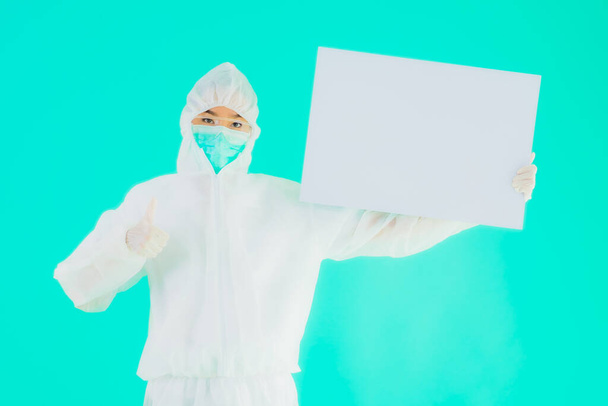 Портрет красива молода азіатська жінка-лікар носить рп або особисте захисне обладнання для захисту від коронавірусу або ковірусу19 з порожньою картковою білою дошкою на синьому ізольованому фоні
 - Фото, зображення