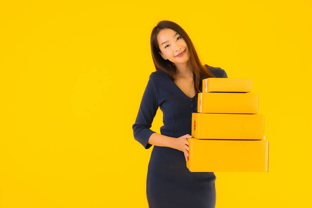 Portrait beautiful young asian woman with cardboard box packkage ready for shipping on yellow isolated background - Foto, Imagem