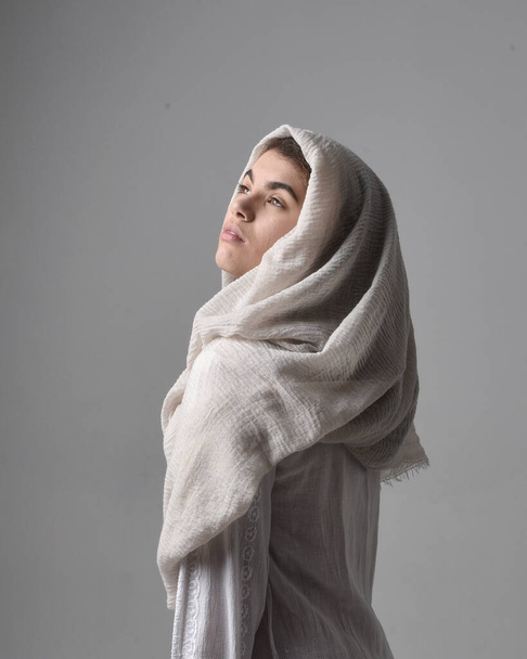 close up  portrait of young woman wearing classical white gown and a head covering veil in biblical style, standing worshiping  pose on light studio background. - Photo, Image