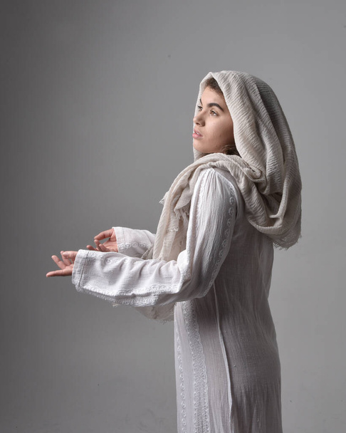 Nahaufnahme Porträt einer jungen Frau in klassischem weißen Gewand und Kopftuch im biblischen Stil, die anbetend auf hellem Studiohintergrund posiert. - Foto, Bild